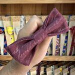 1. Lazo de tela con escritura en tonos burdeos para moda y accesorios infantiles.