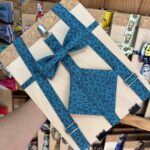Lazo de tela azul con estampado floral y clip de metal, en caja de madera para regalos personalizados.