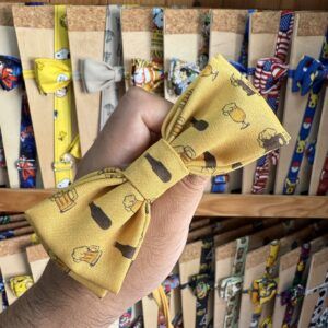 1. La imagen muestra un lazo de tela amarillo con diseños de cervezas, en un puesto de accesorios.