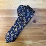 1. Corbata de seda azul con estampado de bandanas en tonos dorados y blancos.