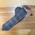 Corbata de lana con patrón de cuadros en tonos grises y rojos, ideal para looks elegantes y formales.