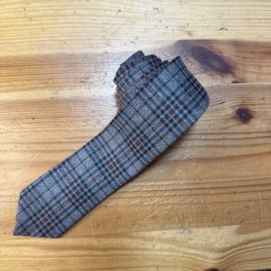 Corbata de lana con patrón de cuadros en tonos grises y rojos, ideal para looks elegantes y formales.