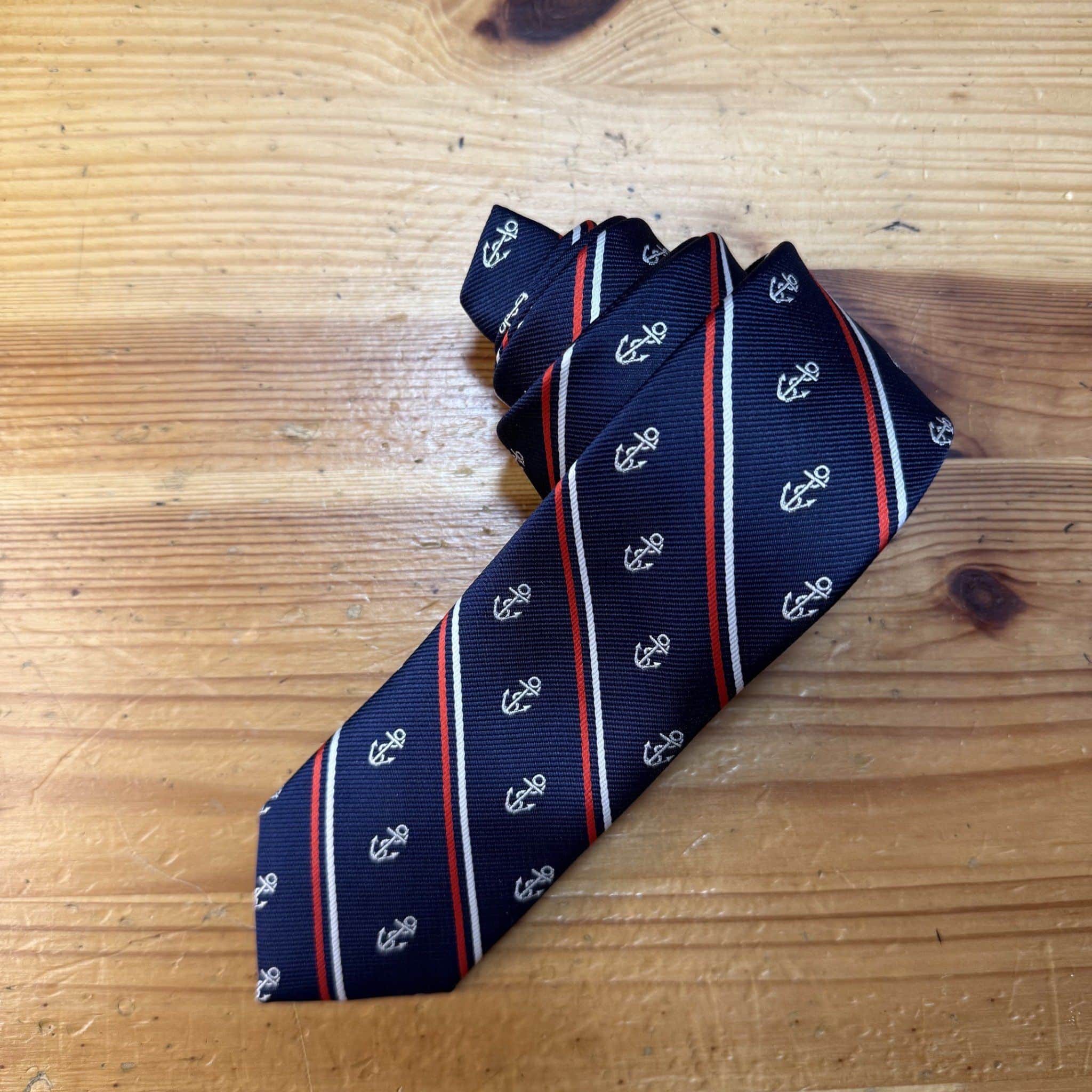 Cámara con corbata azul con anclas blancas y rayas rojas y blancas, estilo náutico elegante.