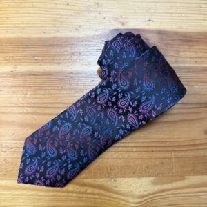 Cinturón de diseño con estampado paisley y flor en tonos morados y rosas sobre fondo negro.