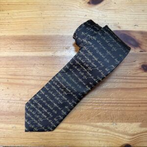 Tacto elegante, bufanda de seda con letras manuscritas en negro y beige en madera natural.
