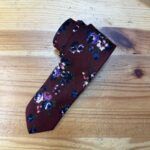 Corbata de seda con estampado floral en tonos morados y azules sobre fondo burdeos elegante y sofisticado.