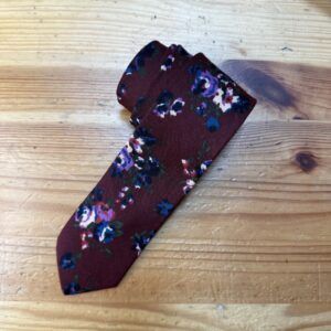 Corbata de seda con estampado floral en tonos morados y azules sobre fondo burdeos elegante y sofisticado.
