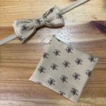Corbata y pañuelo de tela con logo de Carmenatis en tonos neutros, ideal para accesorios de moda y regalos personalizados.