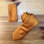 Corbata de satén en color mostaza sobre superficie de madera, elegante y moderna.