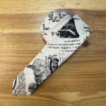 Bucle de tela con estampado vintage de texto y bicicletas, ideal para proyectos de costura y manualidades creativas.