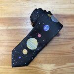 Caminata por el espacio con corbata de planetas y estrellas en fondo negro.