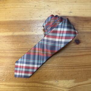 Corbata de tartán azul, rojo y crema sobre mesa de madera.