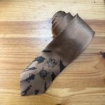 Cinturón de seda con diseño minimalista y personajes de anime en tonos marrón oscuro.
