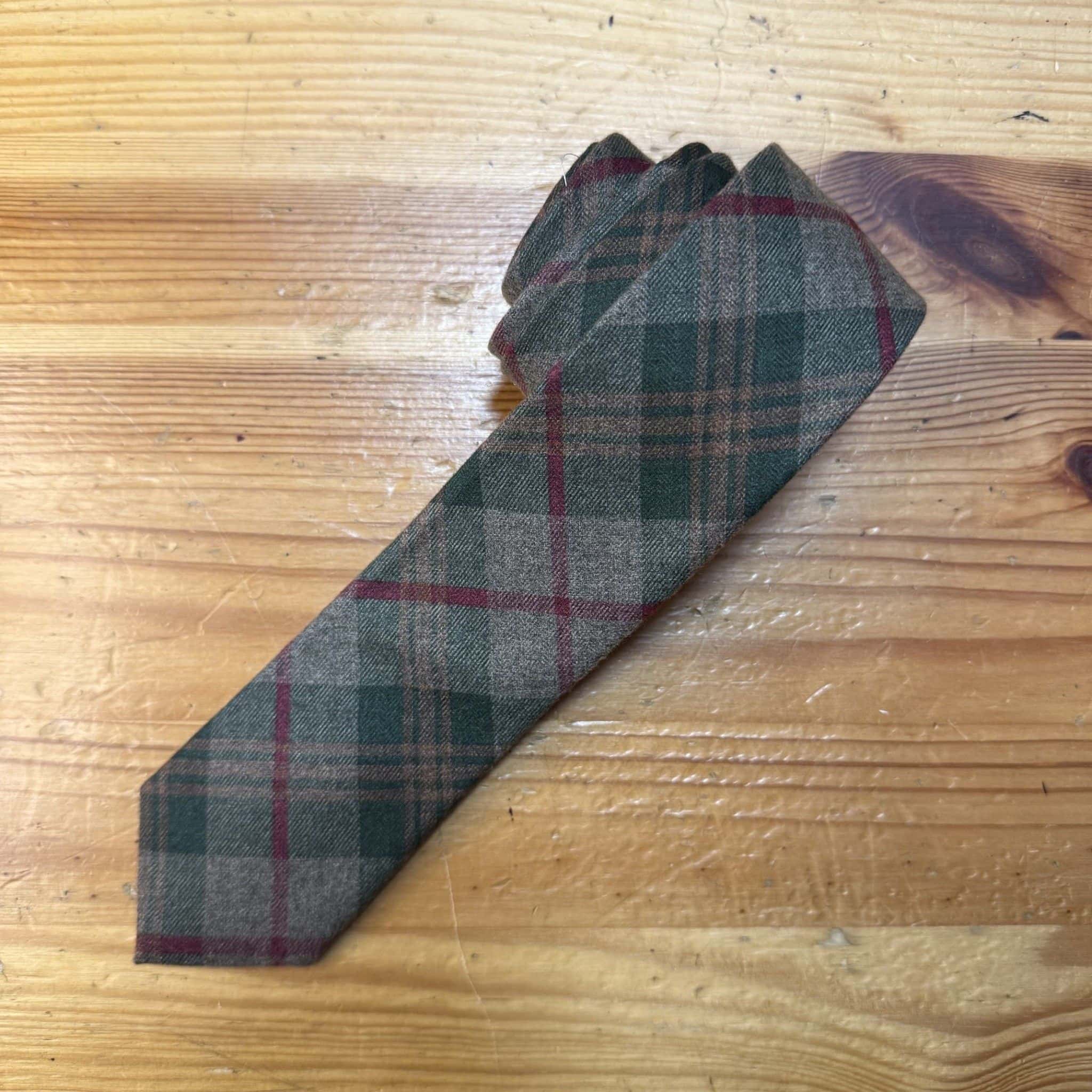 Corbata de lana con estampado de tartán en tonos verde, gris y rojo, ideal para looks clásicos y elegantes.