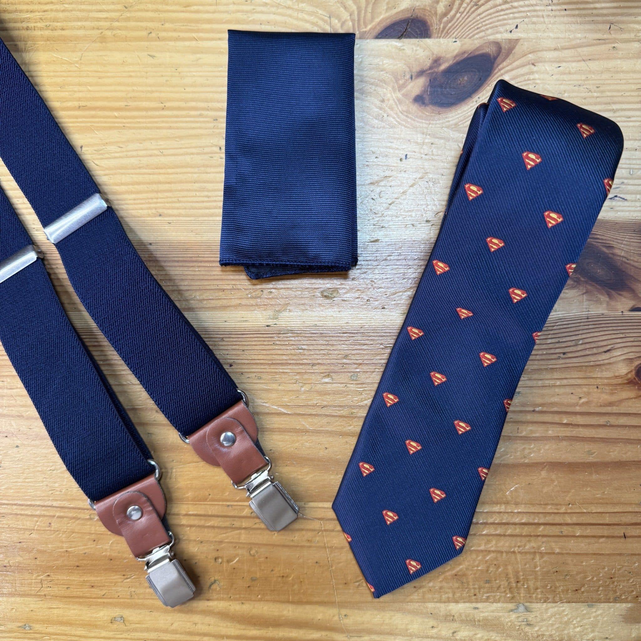 Corbata con logo de Superman y tirantes a juego en color azul oscuro sobre madera.