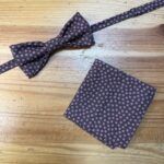 Corbata y pañuelo con estampado de pequeñas flores moradas en fondo negro.