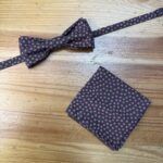 Corbatín y pañuelo a juego en tela con estampado floral rosa sobre fondo negro, accesorios elegantes para hombre.