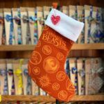 Calcetín de Navidad de "Fabulous Beasts" con diseño de símbolos mágicos y letras en tonos anaranjados, con acabado blanco en la parte superior.