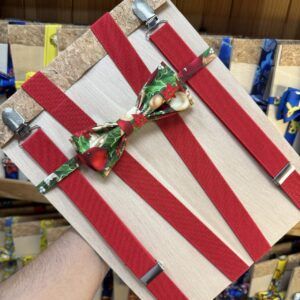Corbata de navidad con lazo decorativo de dibujos navideños, sobre fondo de madera y cinta roja.