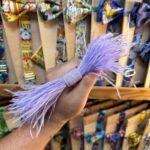 La imagen muestra un mano sosteniendo un lazo de plumas lilas en una tienda de accesorios de moda.