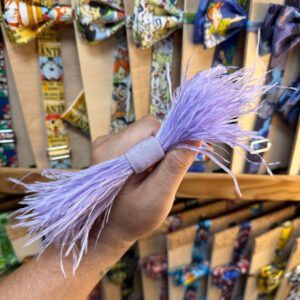 La imagen muestra un mano sosteniendo un lazo de plumas lilas en una tienda de accesorios de moda.