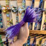 Lazo de cinta y plumas moradas con brillo, ideal para decorar y complementos de moda.